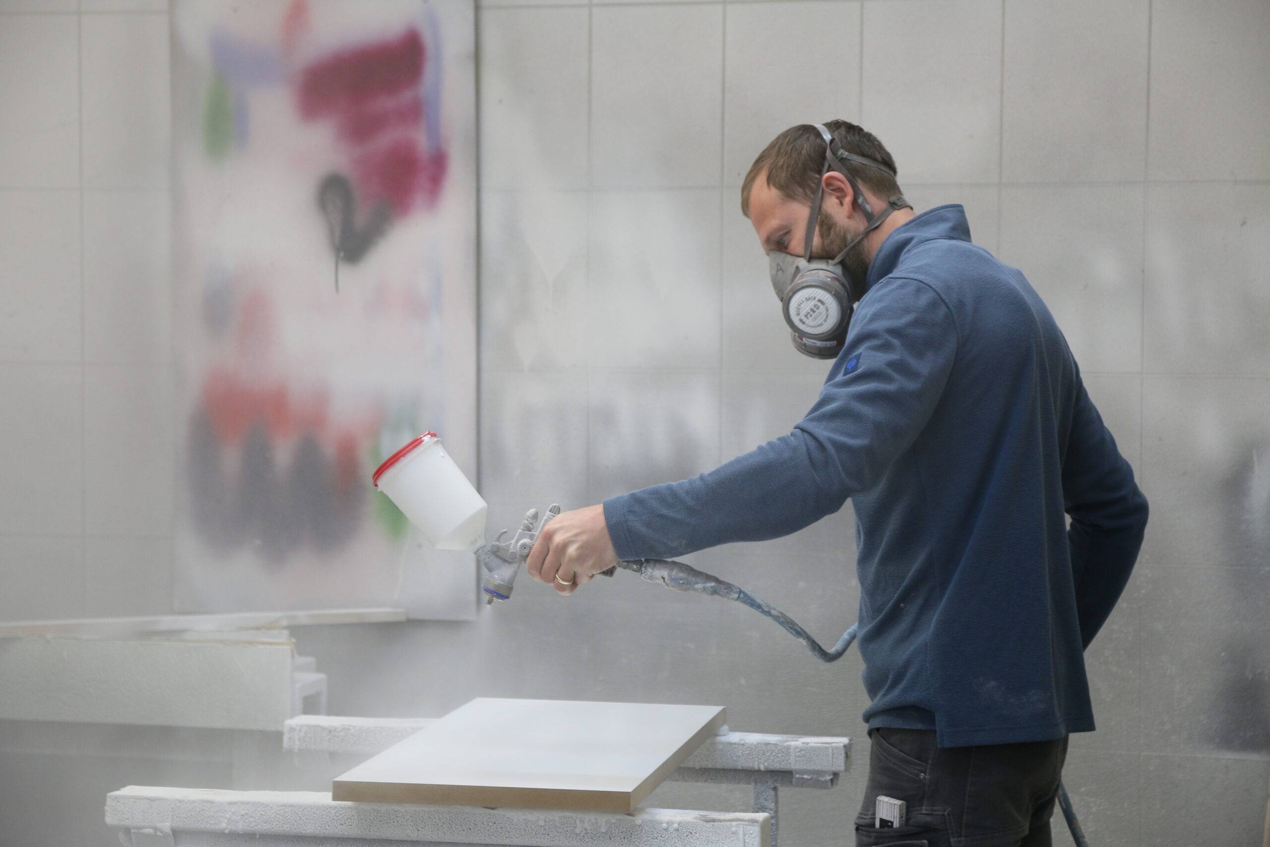 Mann sprüht Farbe auf Oberfläche in Schreiner Werkstatt.